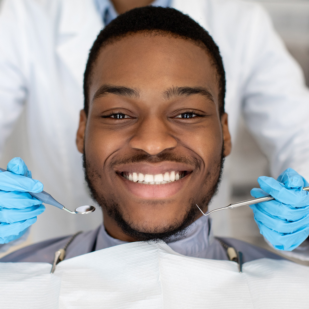 A smiling man wearing blue gloves while sitting in a dental chair with his mouth open for a dental procedure.