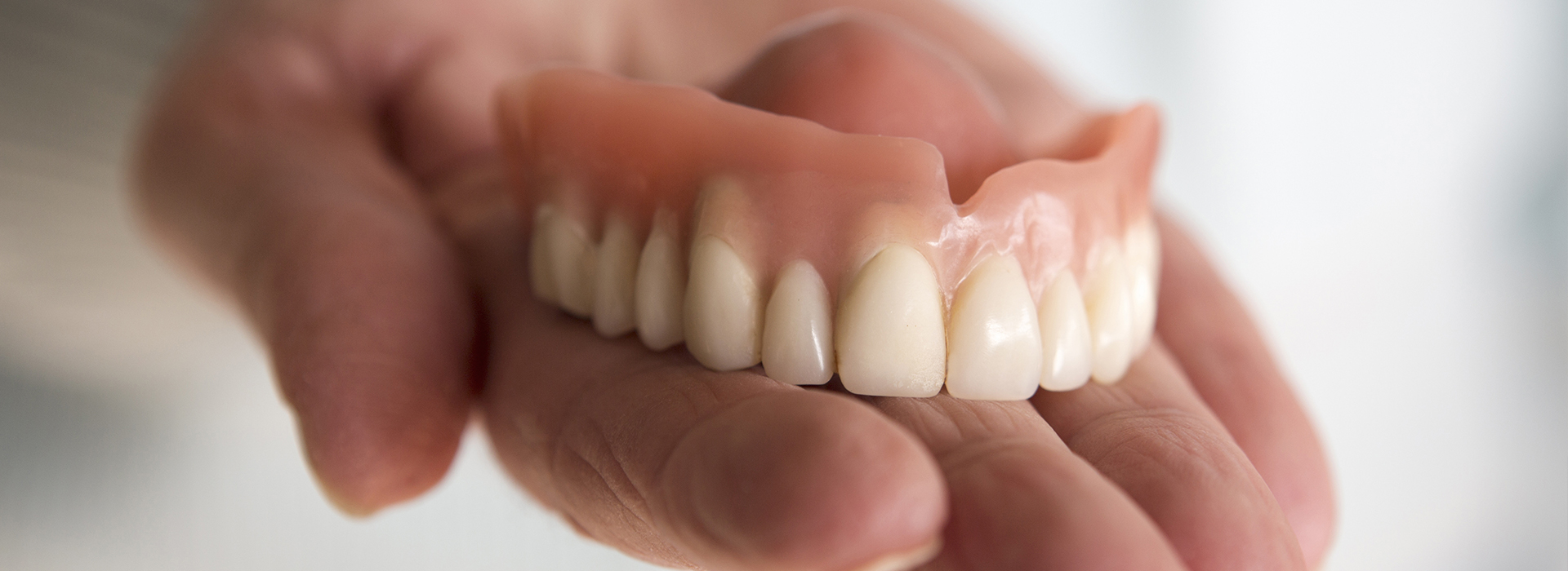 The image shows a person holding an artificial set of teeth with yellowed and missing teeth, which are being held up to showcase their condition.