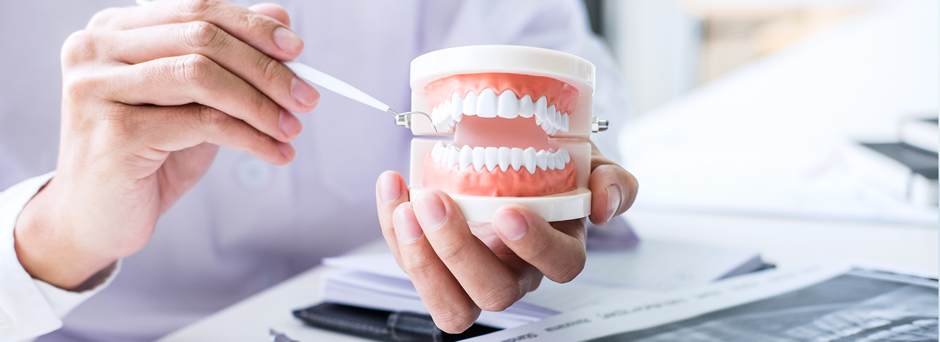 The image shows a person holding a toothbrush with toothpaste, examining a set of teeth in a dental setting, while another individual appears to be taking a photograph with a cell phone.
